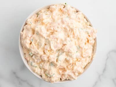 Creamy shrimp dip served in a white bowl, made with small shrimp, cream cheese, and herbs. The chilled seafood dip has a thick, fluffy texture and sits on a light marble surface.