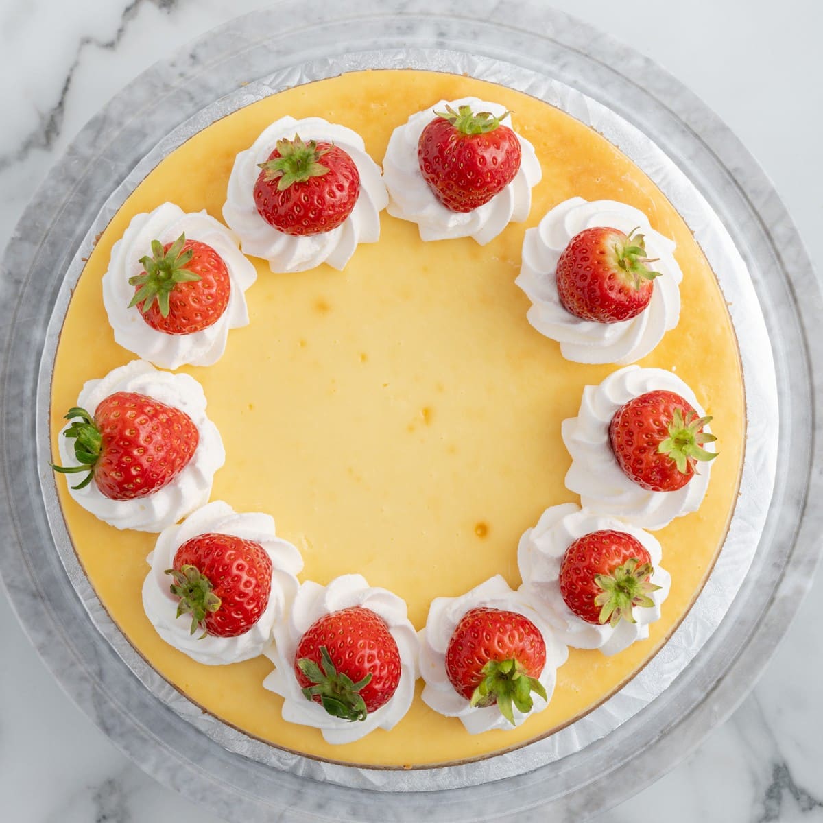 Overhead photo of a decorated Strawberries and Cream Cheesecake topped with piped whipped cream and fresh whole strawberries before slicing and serving.