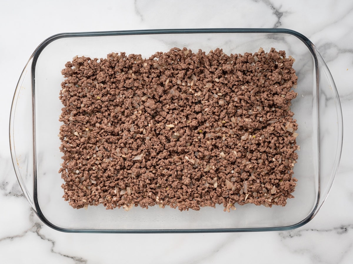 Claude responded: Ground beef and onion mixture spread evenly in a glass baking dish, ready for the sauce layer.Ground beef and onion mixture spread evenly in a glass baking dish, ready for the sauce layer.