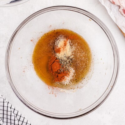 Overhead view of maple syrup, brown sugar, paprika, onion powder, garlic salt, black pepper, and chili powder combined in a glass bowl to make the sweet and savory glaze for Bacon Wrapped Chicken.