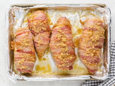 Overhead view of bacon-wrapped chicken breasts on a foil-lined baking sheet sprinkled with brown sugar before baking for sweet and savory Bacon Wrapped Chicken.