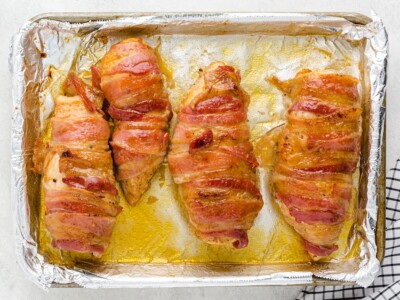 Overhead view of fully baked Bacon Wrapped Chicken on a foil-lined baking sheet with crispy golden bacon and caramelized maple brown sugar glaze ready to serve.