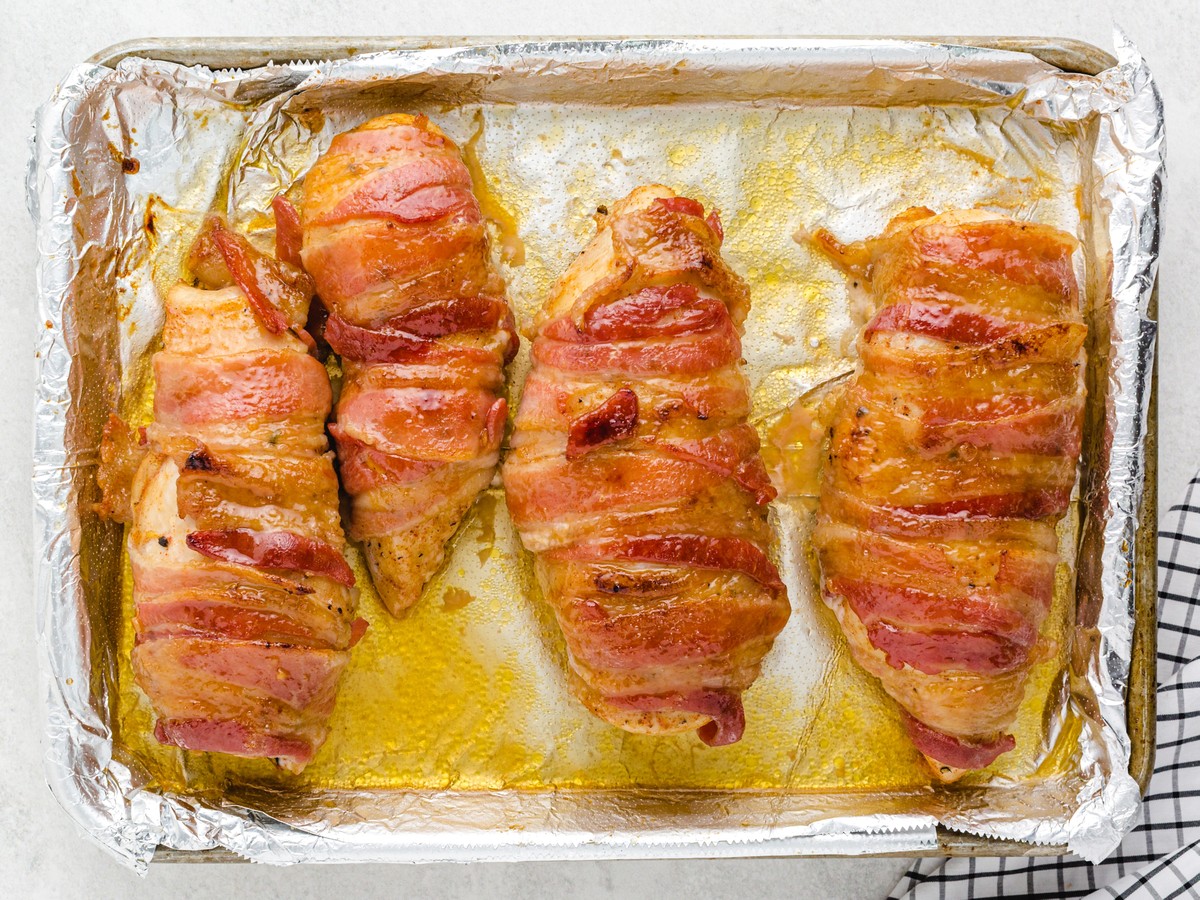 Overhead view of fully baked Bacon Wrapped Chicken on a foil-lined baking sheet with crispy golden bacon and caramelized maple brown sugar glaze ready to serve.