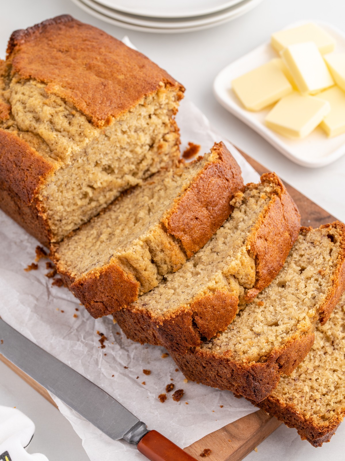 Thick slices of homemade Banana Bread with a golden-brown crust arranged on parchment paper over a wooden board, highlighting the moist, tender crumb and buttery texture.