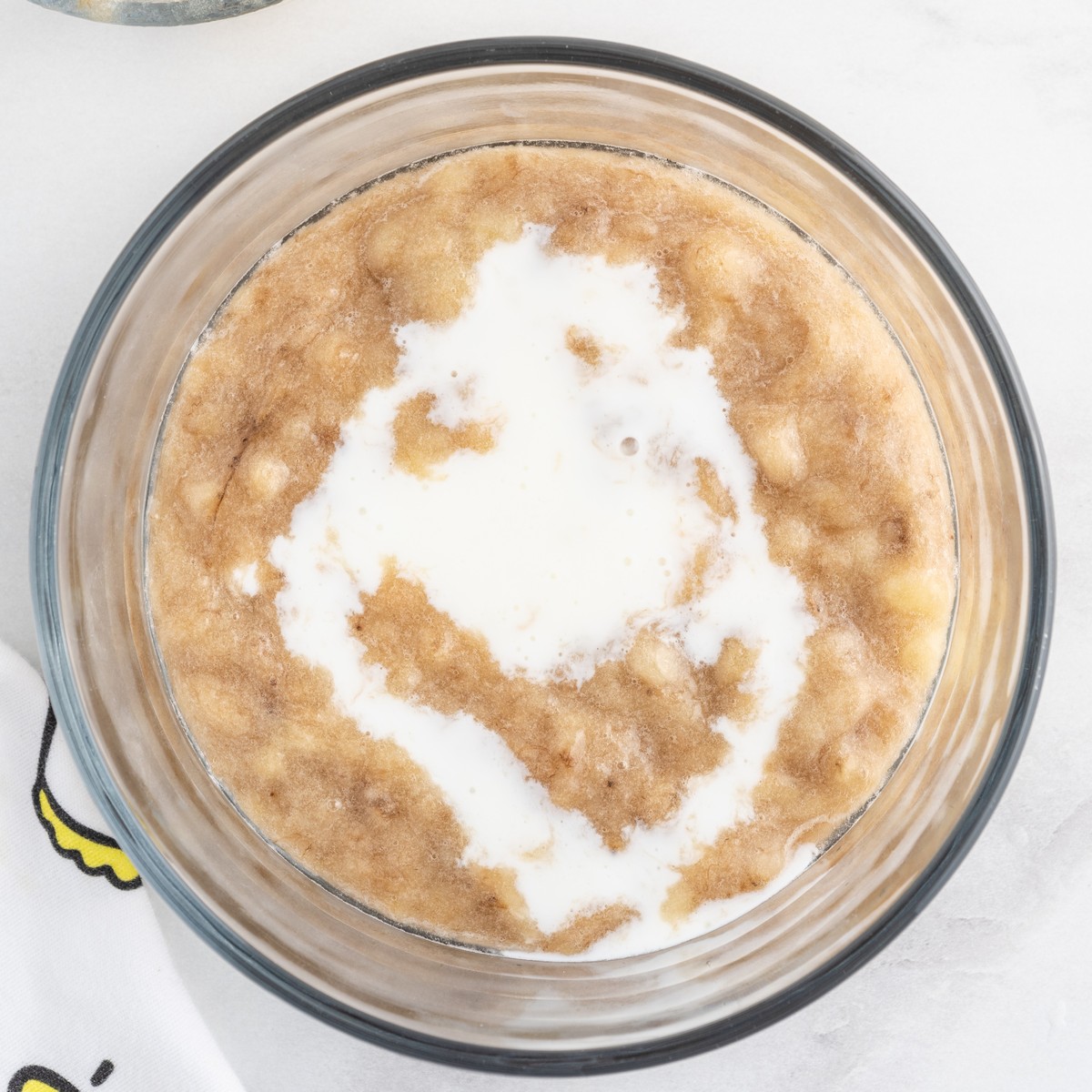 Mashed bananas combined with buttermilk in a glass mixing bowl for Banana Bread, creating the wet ingredient mixture before it is added to the batter.