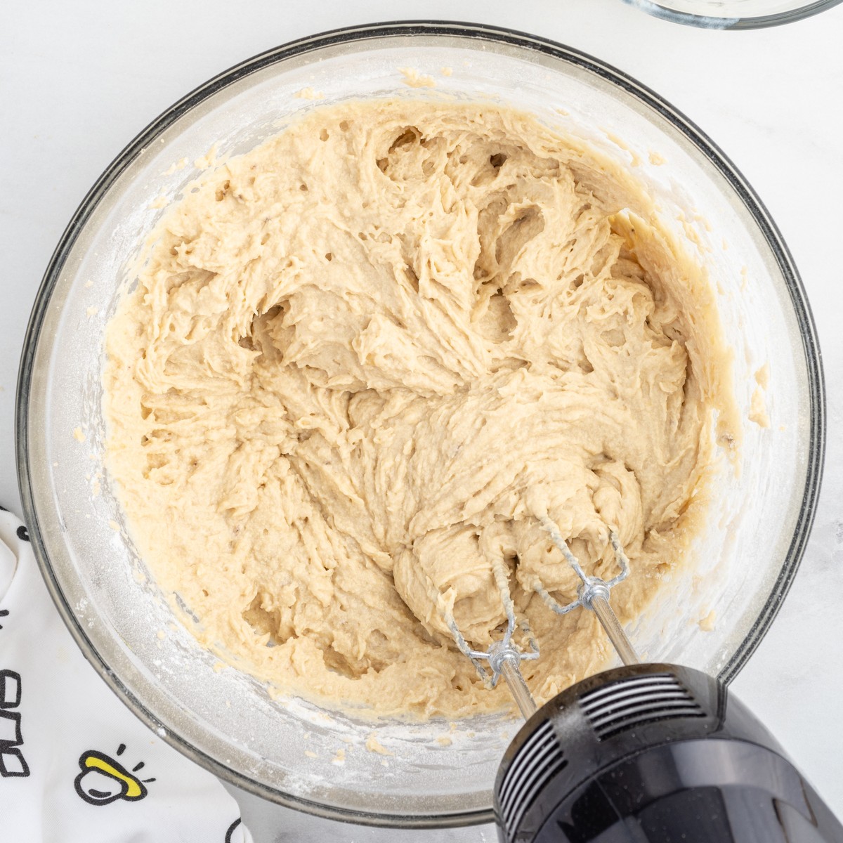 Banana Bread batter fully mixed in a large glass bowl with an electric hand mixer, showing a thick, smooth batter ready to be transferred to a loaf pan for baking.