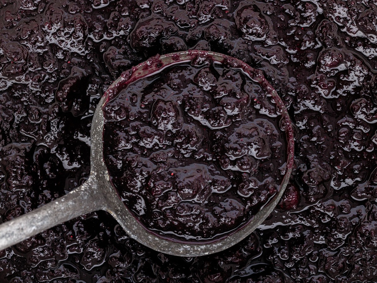 Close-up overhead view of rich homemade Blueberry Butter with visible blueberry pieces in a measuring cup, highlighting its thick, glossy texture.