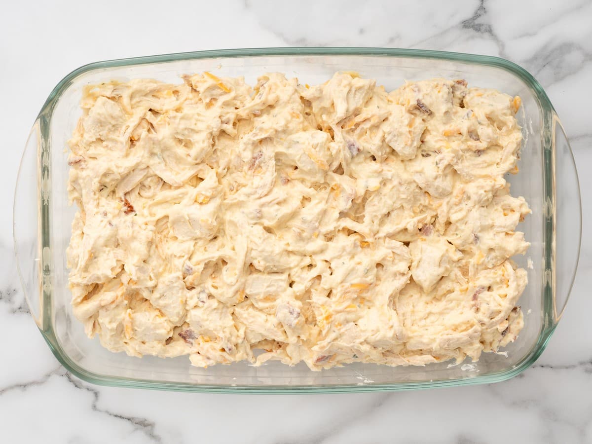 Overhead view of the creamy Chicken Bubble Biscuit Bake mixture spread evenly in a rectangular glass casserole dish before adding the cheese topping.