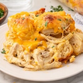 Serving of Chicken Bubble Biscuit Bake with creamy shredded chicken, fluffy biscuit pieces, melted cheddar cheese, bacon, and chopped parsley on a white plate.