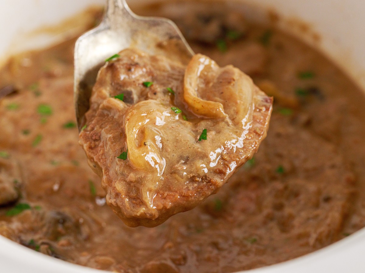 Close-up of tender Crock Pot Cube Steak lifted from the slow cooker, coated in rich mushroom and onion gravy and garnished with chopped parsley.