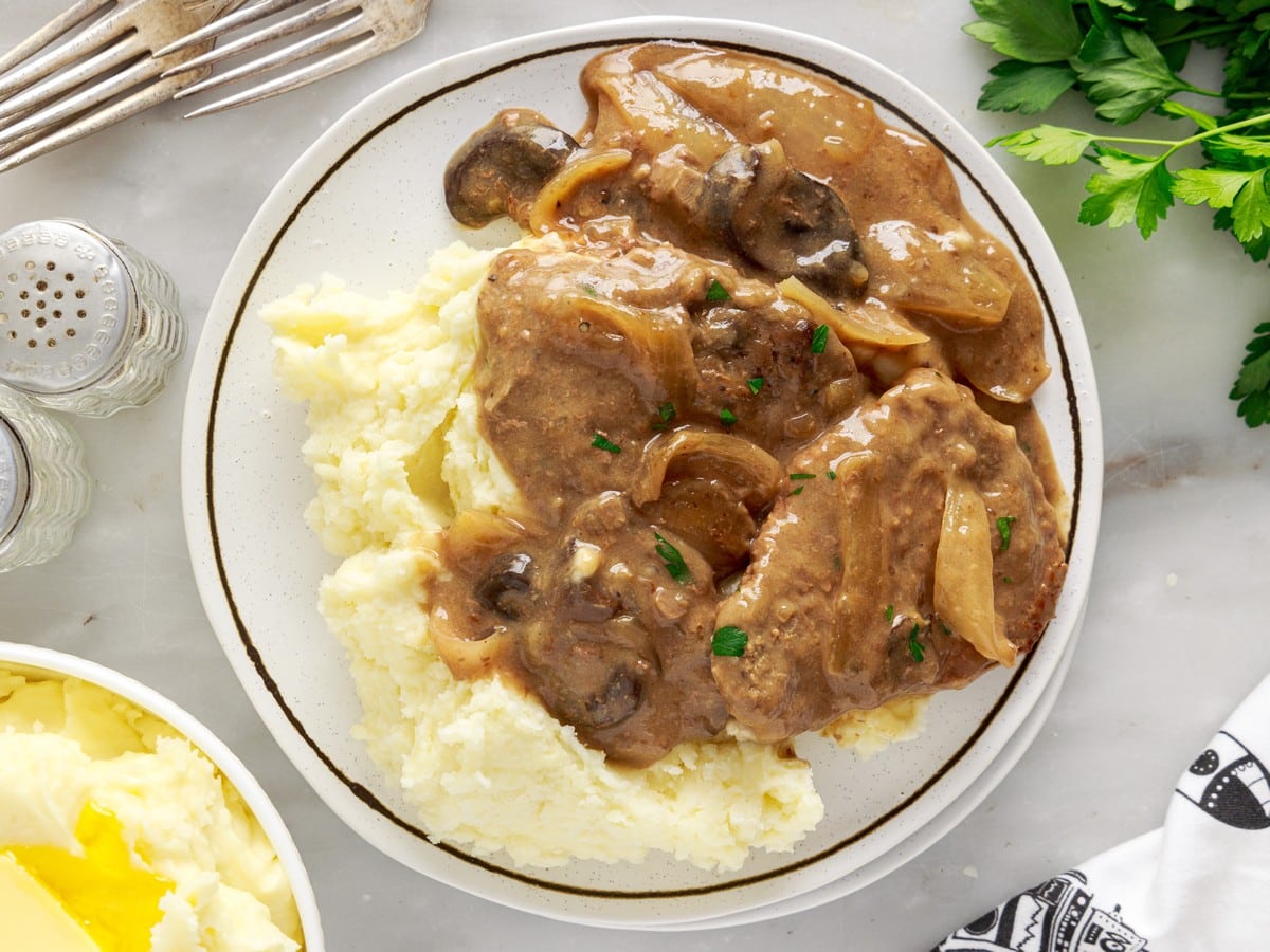 Overhead view of Crock Pot Cube Steak served with creamy mashed potatoes, sliced mushrooms, tender onions, savory brown gravy, and chopped parsley.