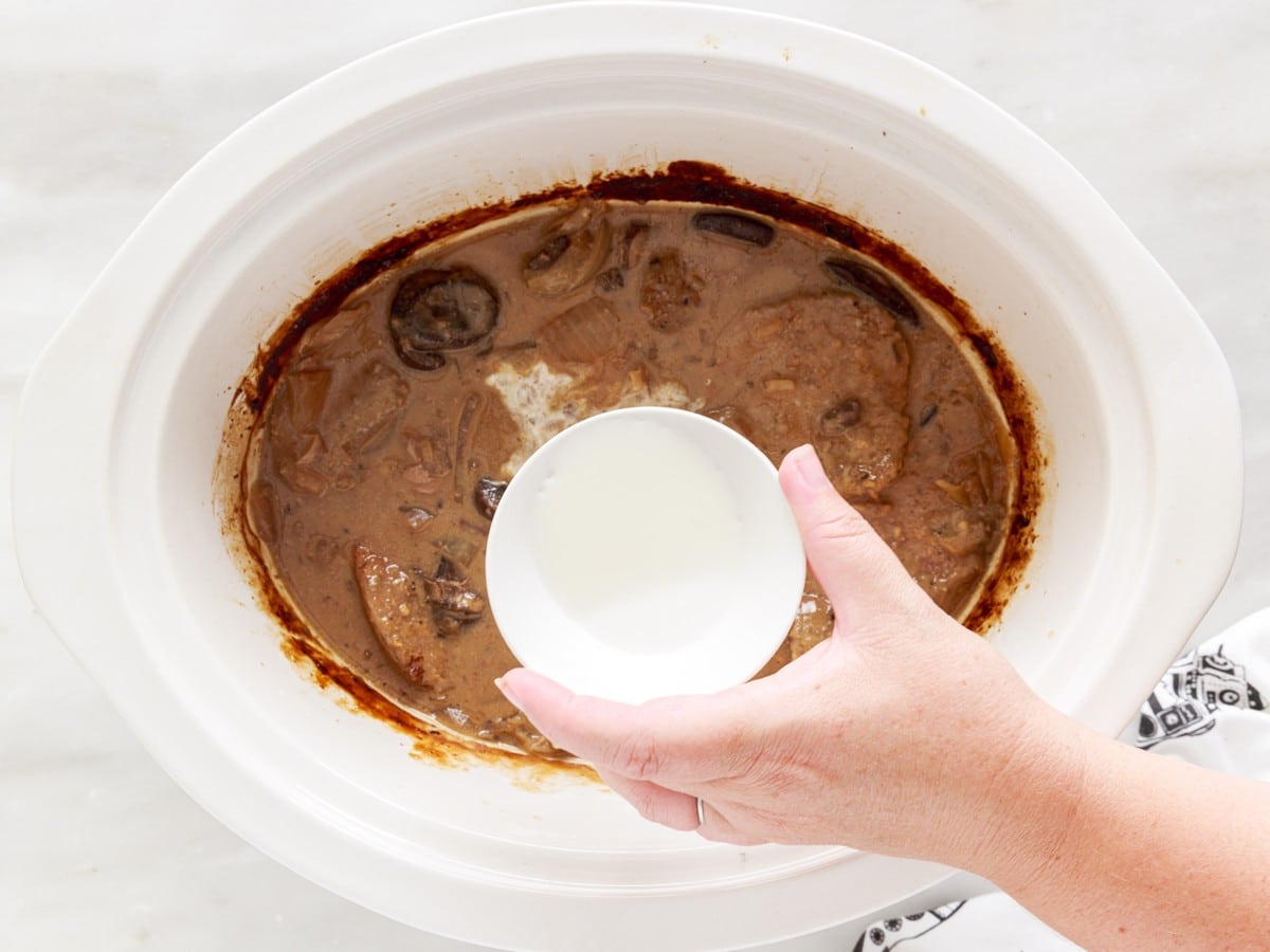 Overhead view of cooked Crock Pot Cube Steak as a cornstarch slurry is added to the mushroom and onion gravy to help thicken the sauce.