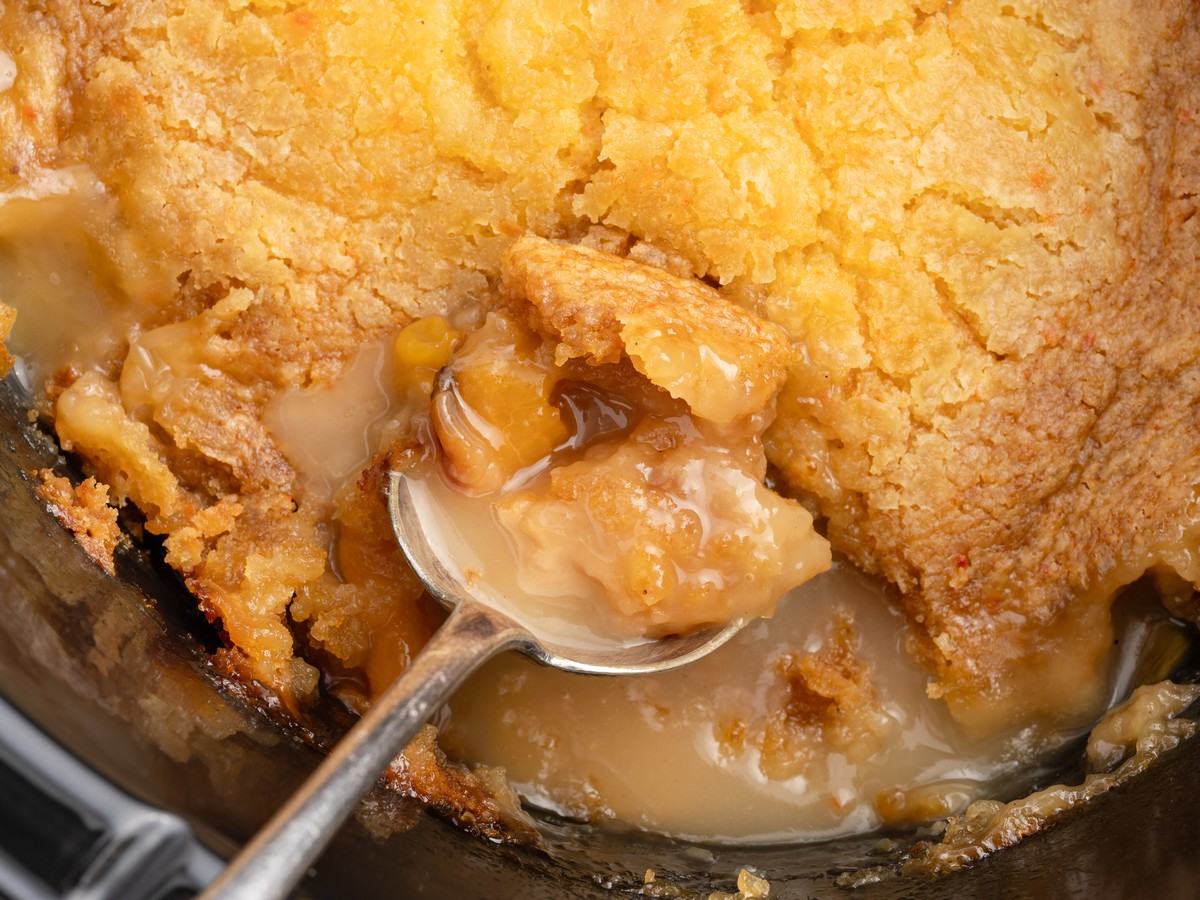 Close-up of Crockpot Peach Dump Cake showing warm peach filling and syrupy sauce under a golden cake mix topping on a spoon.