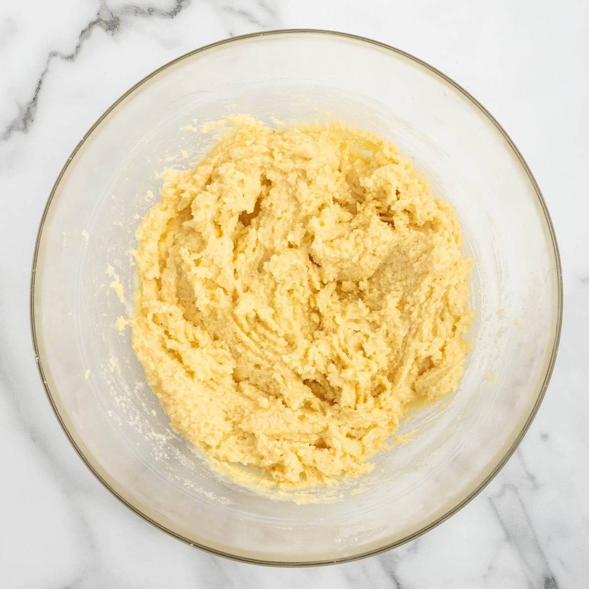 Overhead view of the buttery yellow cake mixture combined with melted butter and ground nutmeg in a large glass mixing bowl for Crockpot Peach Dump Cake.
