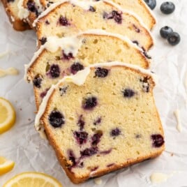 Slices of Lemon Blueberry Pound Cake topped with a thick homemade lemon glaze, showcasing a soft buttery crumb filled with juicy blueberries and served with fresh lemon wedges.