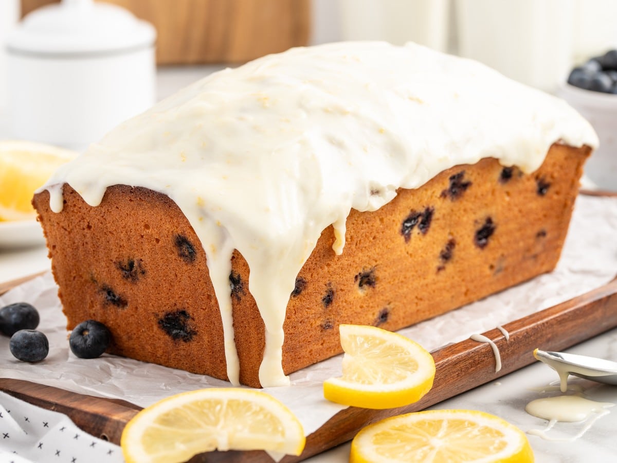 Homemade Lemon Blueberry Pound Cake generously coated with thick lemon glaze, allowing the icing to drip naturally over the sides of the loaf before slicing.