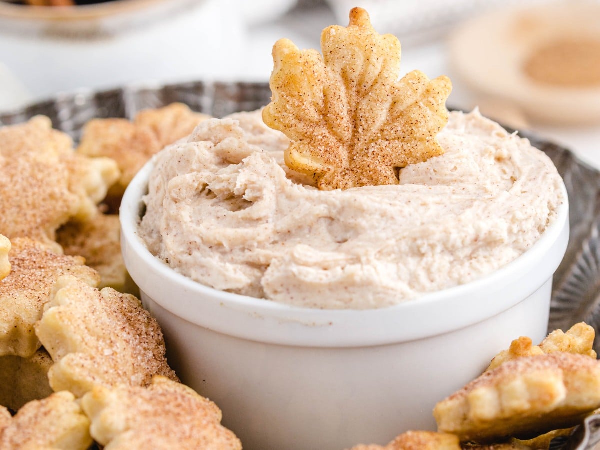 Close-up of creamy cinnamon dip topped with a leaf-shaped cinnamon-sugar pie crust chip and surrounded by crisp pie crust chips.