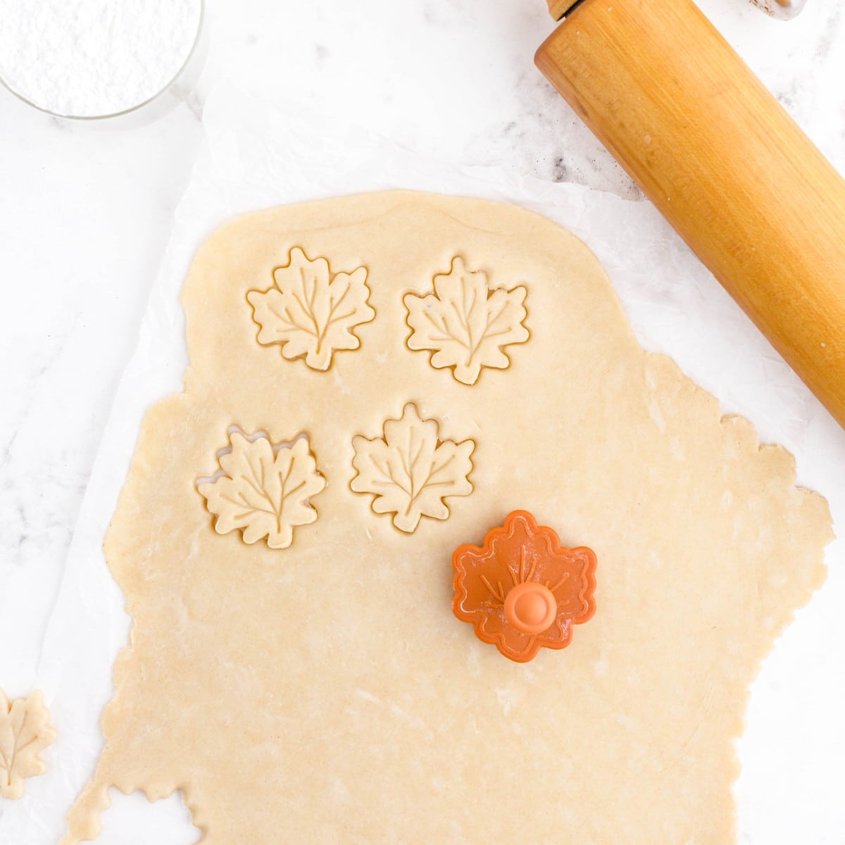 Overhead view of rolled pie crust dough being cut into leaf shapes with an orange cutter for Pie Crust Chips with Cinnamon Dip.