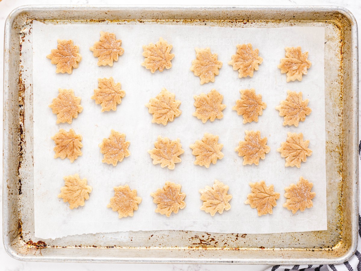 Leaf-shaped pie crust chips sprinkled with cinnamon sugar and arranged on a parchment-lined baking sheet before baking.