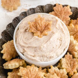 Cinnamon-sugar pie crust chips shaped like autumn leaves arranged around a bowl of creamy cinnamon dip on a dark decorative platter.