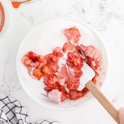Crushed fresh strawberries mixed with granulated sugar in a large bowl as the first step in making homemade Strawberry Freezer Jam.