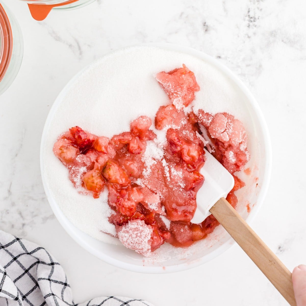 Crushed fresh strawberries mixed with granulated sugar in a large bowl as the first step in making homemade Strawberry Freezer Jam.