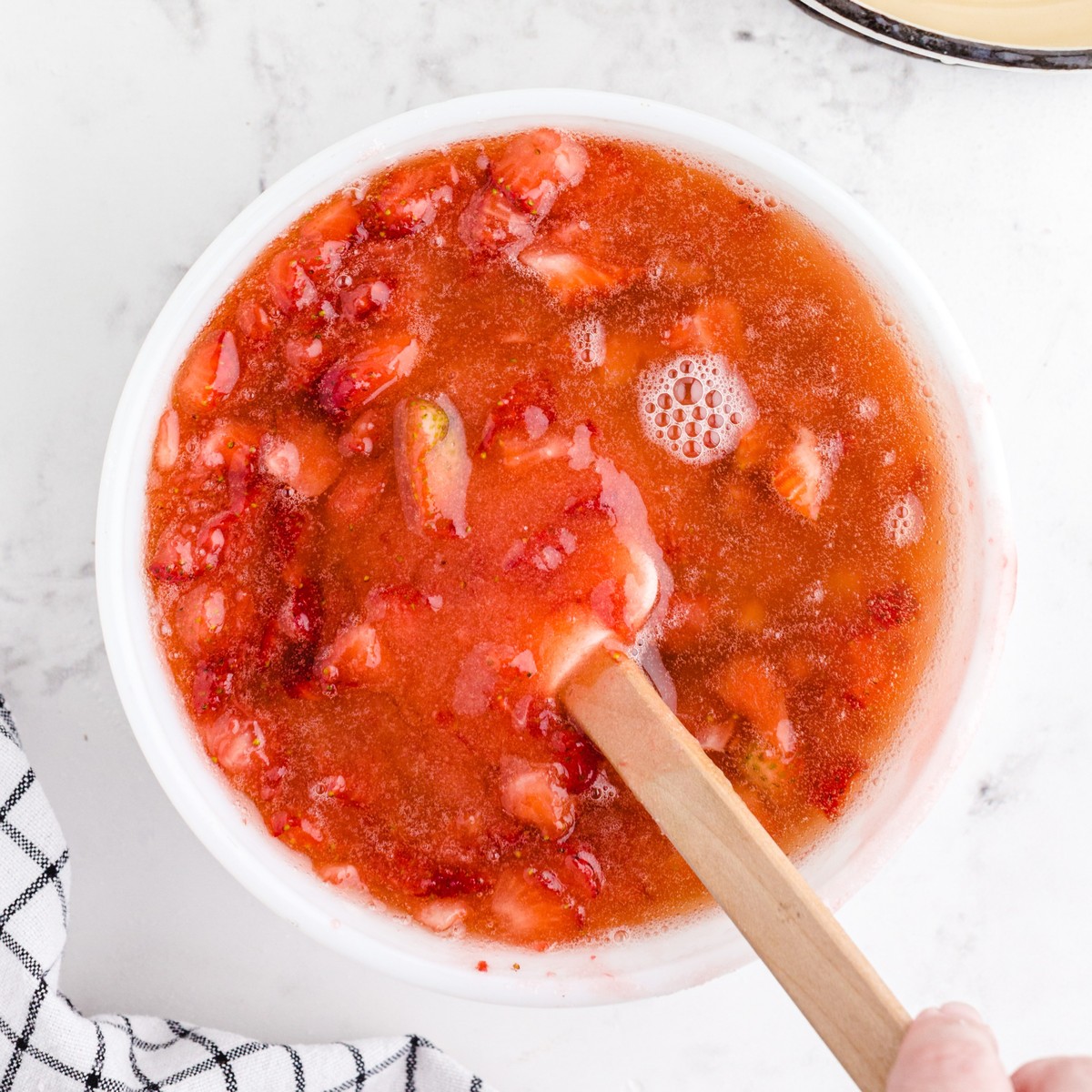 Hot dissolved fruit pectin stirred into the sweetened crushed strawberries until the mixture is smooth and well combined for homemade Strawberry Freezer Jam.