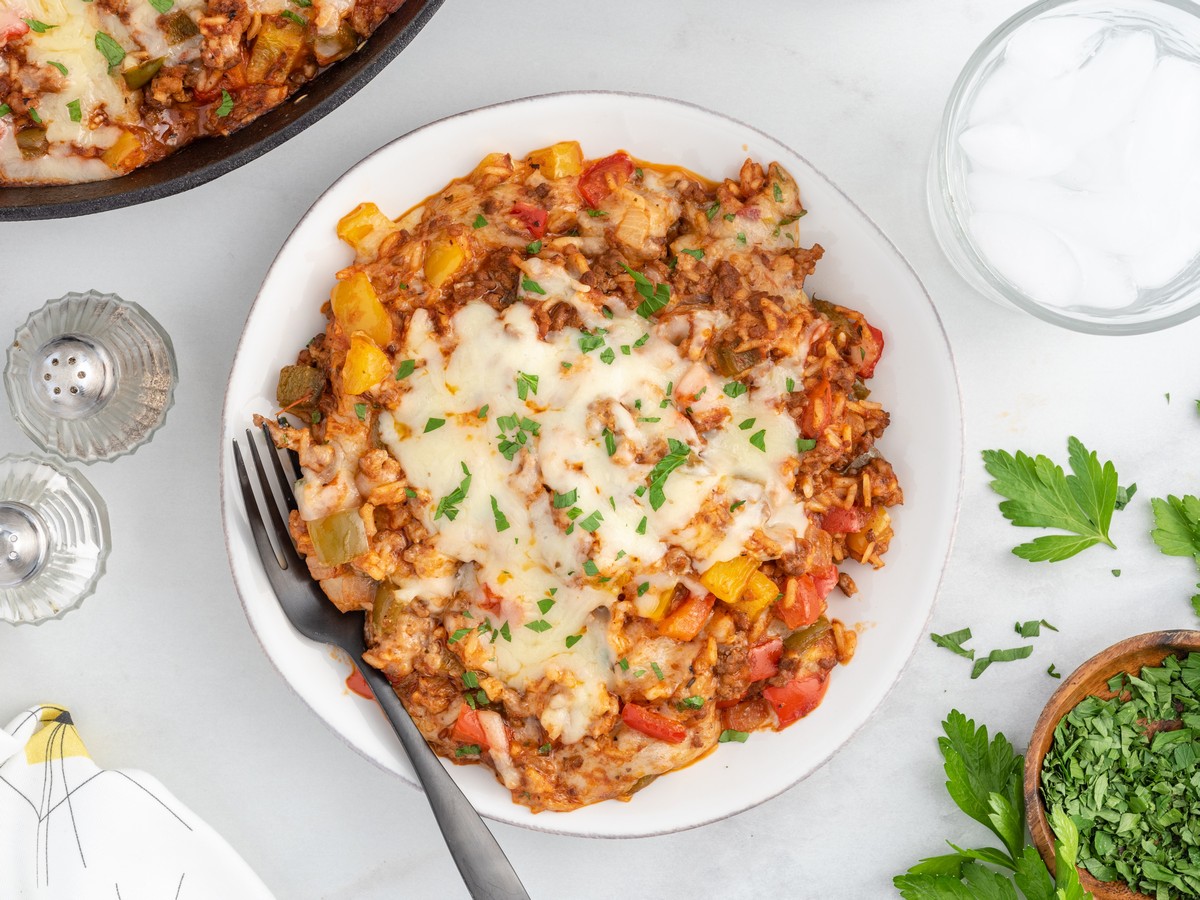 Overhead view of a plated serving of Stuffed Pepper Casserole topped with melted mozzarella, seasoned ground beef, rice, colorful bell peppers, and fresh parsley.