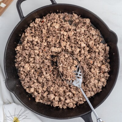 Overhead view of browned ground beef and Italian sausage cooking in a cast iron skillet, the first step for making Stuffed Pepper Casserole.