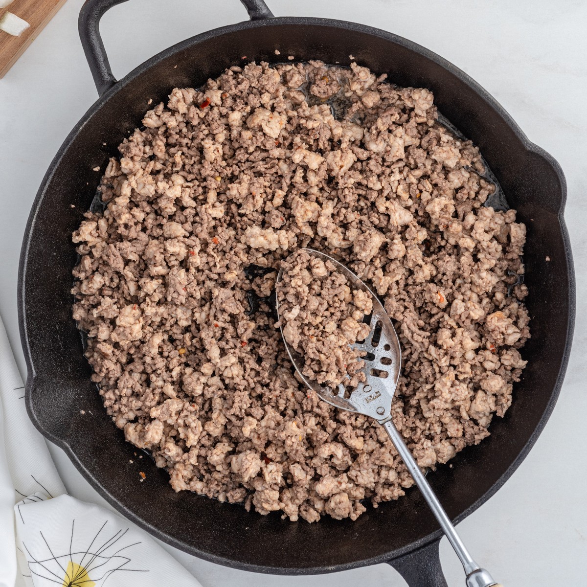 Overhead view of browned ground beef and Italian sausage cooking in a cast iron skillet, the first step for making Stuffed Pepper Casserole.