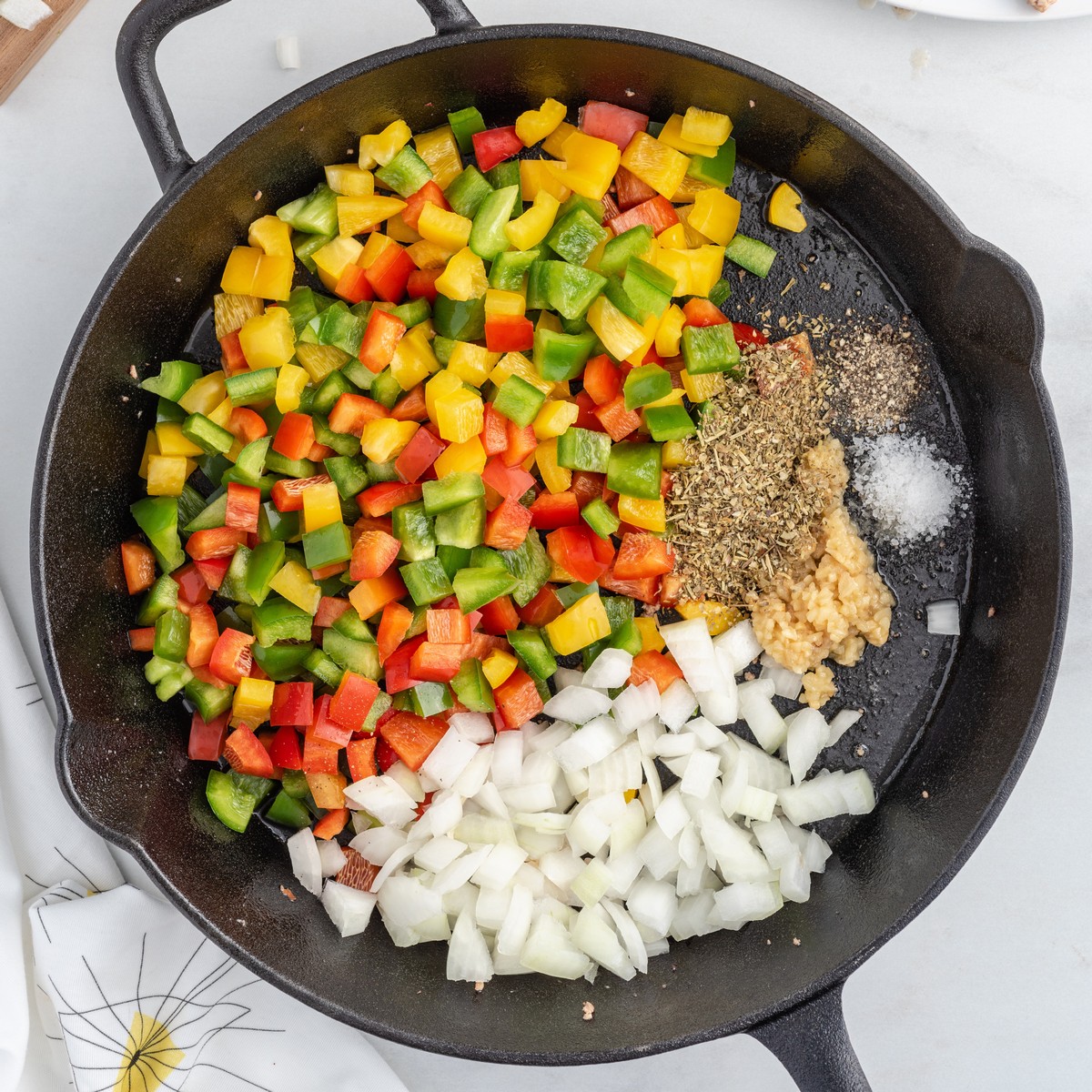 Diced red, yellow, and green bell peppers, chopped onion, garlic, Italian seasoning, salt, and pepper added to a cast iron skillet for Stuffed Pepper Casserole before cooking.