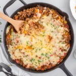 Wooden spoon lifting a cheesy serving of Stuffed Pepper Casserole from a cast iron skillet topped with melted Monterey Jack cheese and fresh parsley.
