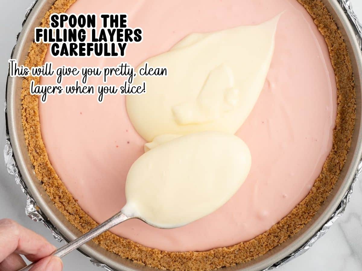 Spooning vanilla cheesecake batter in dollops over a pink strawberry layer in a foil-wrapped springform pan, a technique that keeps the layers clean and distinct after baking.