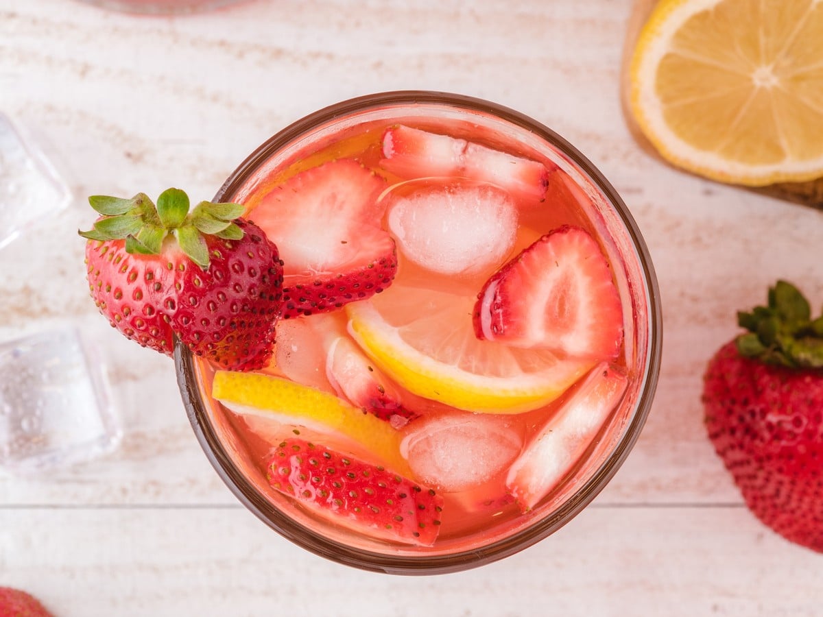 Overhead view of a glass of Strawberry Lemonade with ice, sliced strawberries, lemon slices, and a fresh strawberry garnish for a refreshing summer drink.