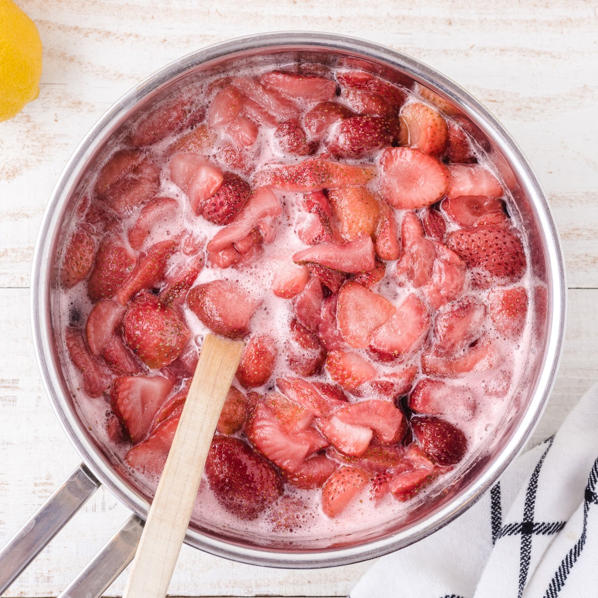 Strawberries simmering in a saucepan with sugar and water while being stirred to make fresh strawberry syrup for Strawberry Lemonade.