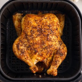 Top-down view of a finished Air Fryer Whole Chicken in the air fryer basket with deeply golden, seasoned skin and crisp roasted edges.