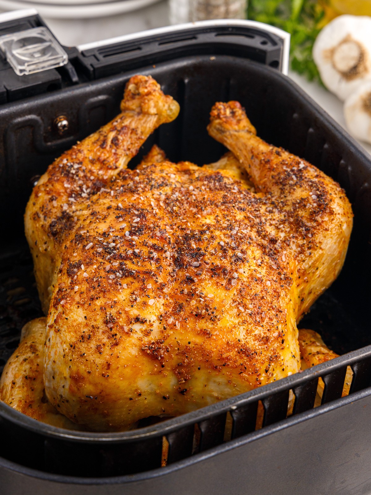 Close-up of a golden-brown Air Fryer Whole Chicken with crisp, seasoned skin resting inside a black air fryer basket.