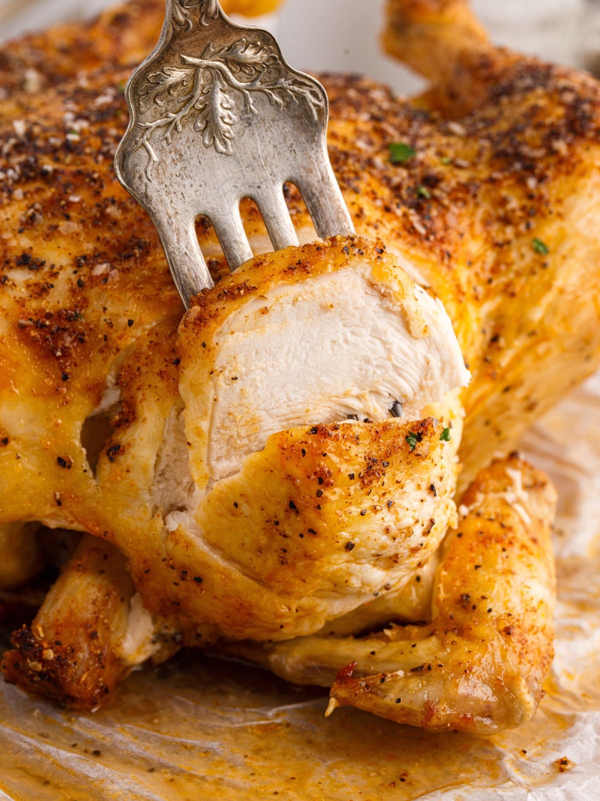 Close-up of sliced Air Fryer Whole Chicken breast showing juicy white meat beneath golden seasoned skin, with a serving fork lifting a thick slice from the roasted chicken.