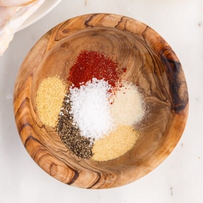Overhead view of the seasoning mixture for Air Fryer Whole Chicken, with paprika, coarse salt, black pepper, garlic powder, onion powder, and seasoned salt arranged in a wooden bowl.