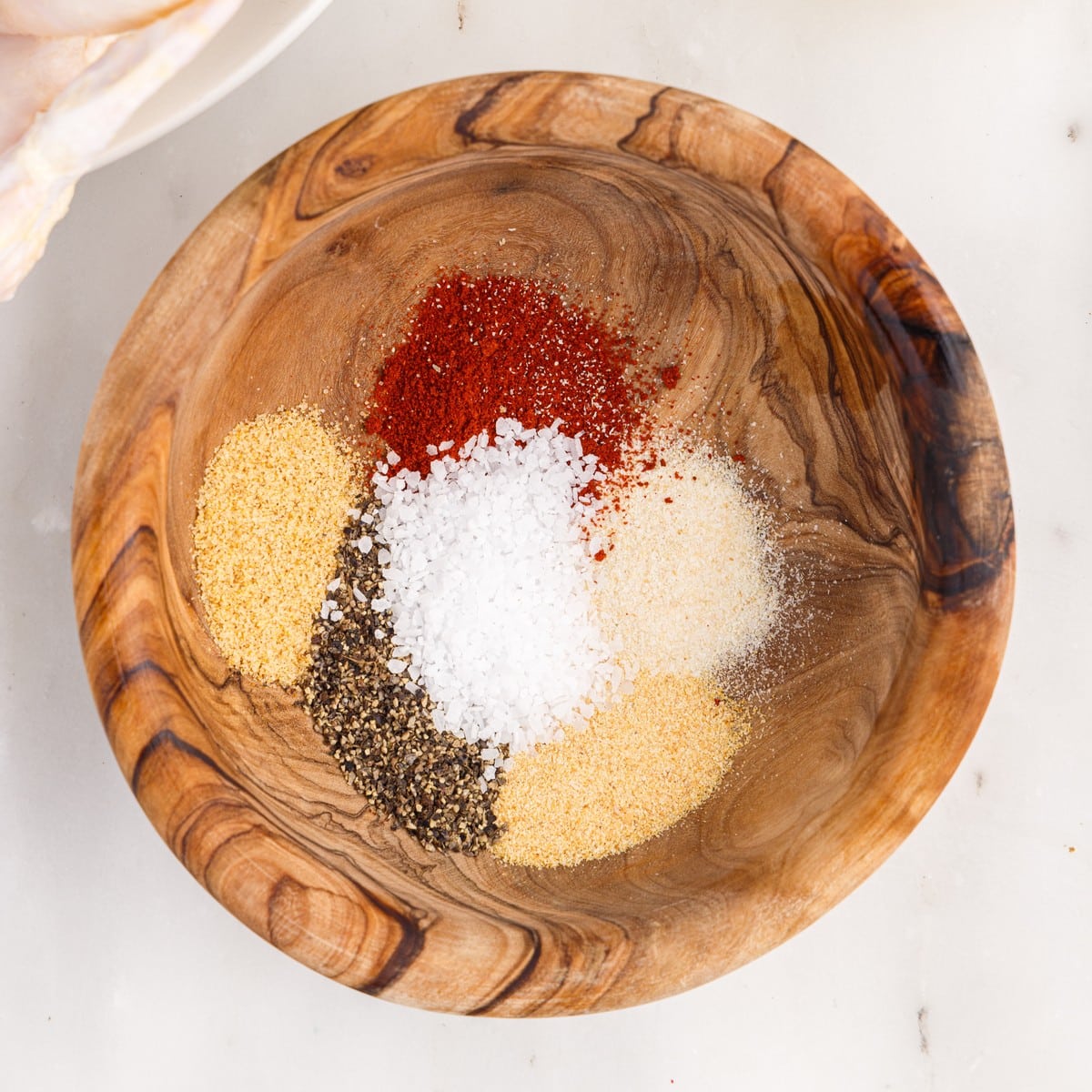 Overhead view of the seasoning mixture for Air Fryer Whole Chicken, with paprika, coarse salt, black pepper, garlic powder, onion powder, and seasoned salt arranged in a wooden bowl.