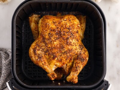 Overhead view of a golden-brown Air Fryer Whole Chicken resting in the black air fryer basket, with crisp seasoned skin and browned edges.