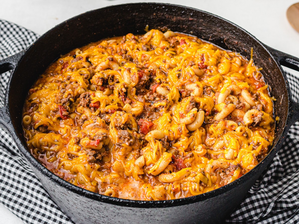 Close-up of homemade American Chop Suey in a black cast-iron skillet, made with elbow macaroni, seasoned ground beef, tomatoes, and melted cheddar cheese.