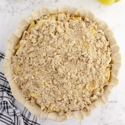 Overhead view of an unbaked Caramel Apple Pie topped generously with a crumbly streusel mixture, with the crimped pie crust visible around the edges.