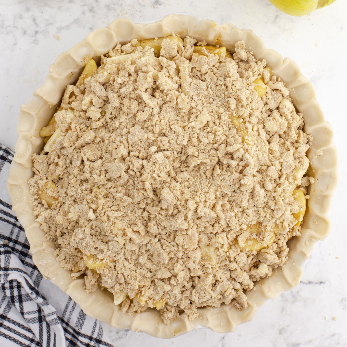 Overhead view of an unbaked Caramel Apple Pie topped generously with a crumbly streusel mixture, with the crimped pie crust visible around the edges.