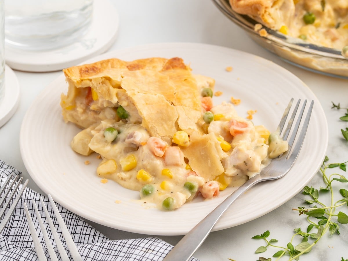 Slice of homemade Chicken Pot Pie served on a white plate with flaky golden crust, creamy chicken filling, carrots, peas, and corn.
