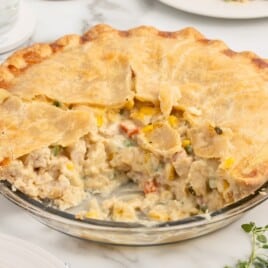 Homemade Chicken Pot Pie in a glass pie dish with a golden, flaky double crust and a creamy filling of chicken, corn, peas, and carrots, with one slice removed.