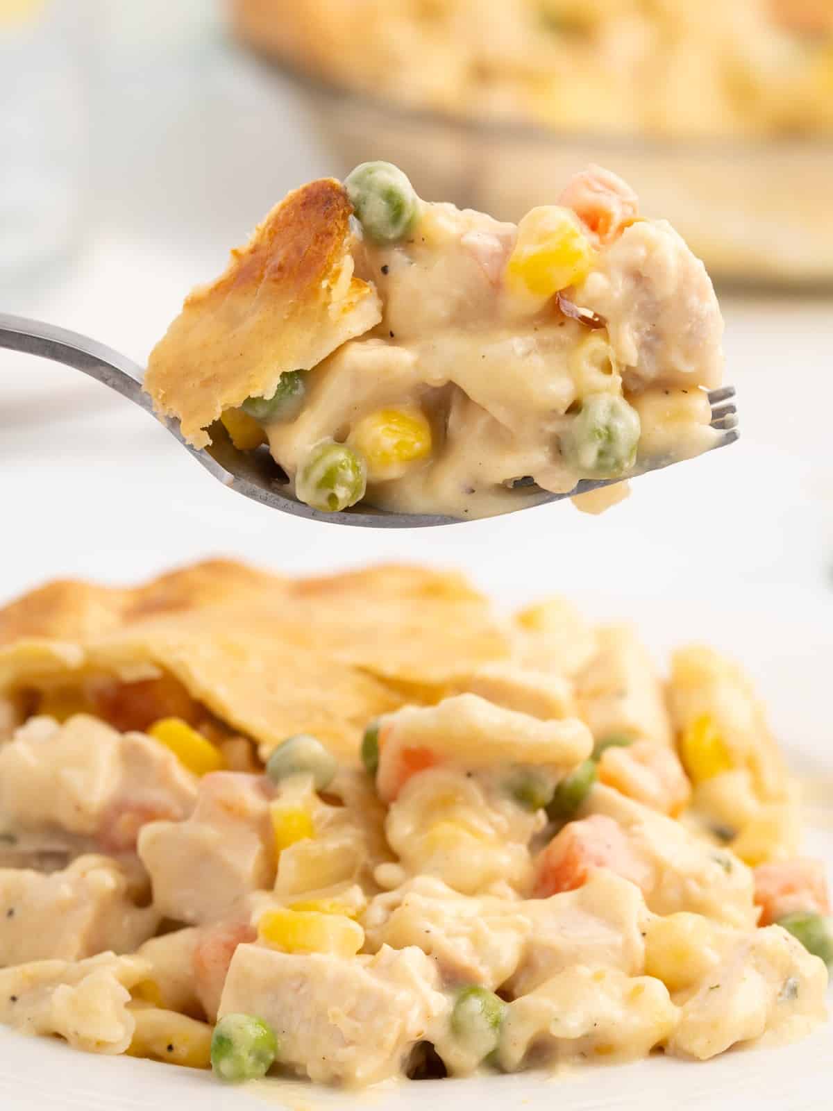 Forkful of creamy Chicken Pot Pie filling with chicken, peas, carrots, corn, and flaky golden crust held above a serving on a white plate.