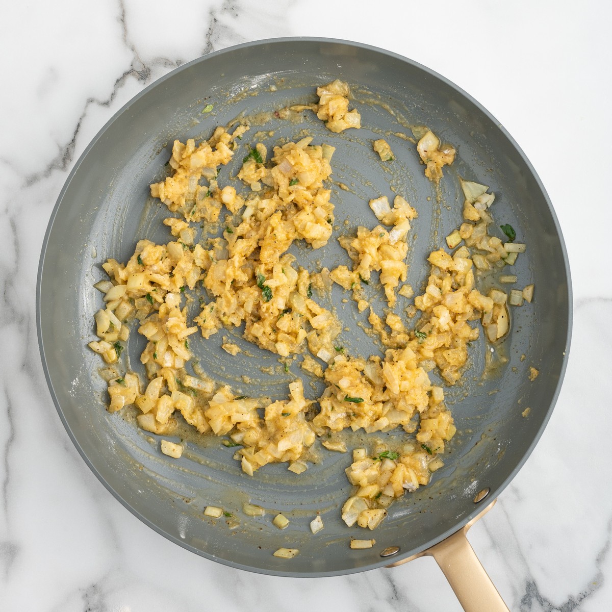 Overhead view of diced onions and fresh thyme cooking with butter, flour, and seasonings in a skillet while preparing the sauce for Chicken Pot Pie.
