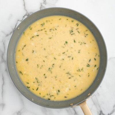 Overhead view of creamy chicken gravy with softened onions and thyme simmering in a skillet for homemade Chicken Pot Pie.