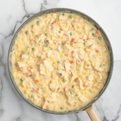 Overhead view of the finished creamy Chicken Pot Pie filling in a skillet with chunks of chicken, peas, carrots, corn, onions, and herbs.